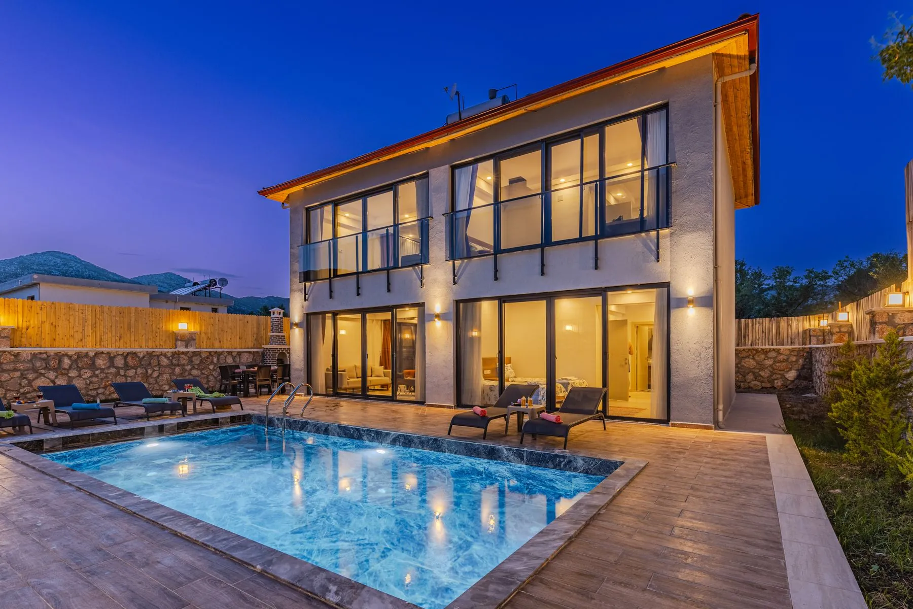 A white two-storey house with a lit pool at twilight